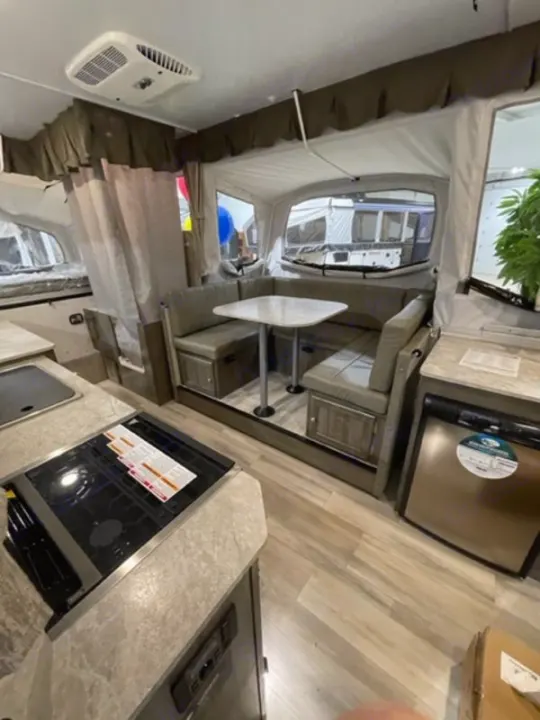 RV rental interior: dinette, kitchen stove, fridge, AC, and a pop-out bed area visible.. Forest River Rockwood Premier 2022