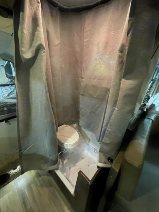Compact RV rental wet bath with toilet in shower pan, enclosed by shower curtain. Toilet is wrapped in plastic.. Forest River Rockwood Premier 2022