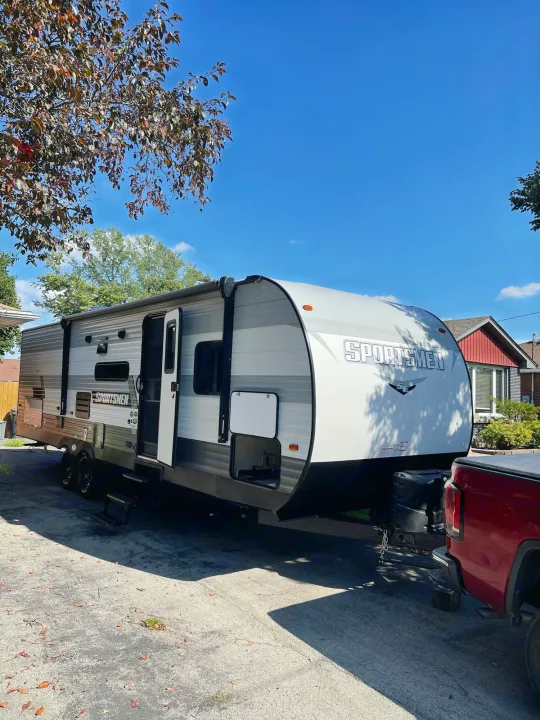 Spacious Sportsmen travel trailer, hooked to a red truck, perfect for your next RV rental. Awning extended, door open.. K-Z Manufacturing Sportsman Classic 2022