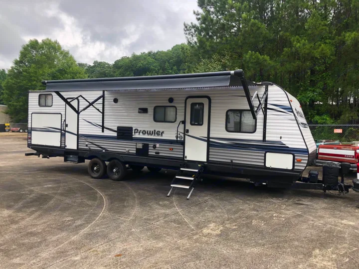 This Prowler travel trailer, ideal for an RV rental, is shown with its awning extended and steps down, parked on asphalt.. Heartland RVs Prowler 2020