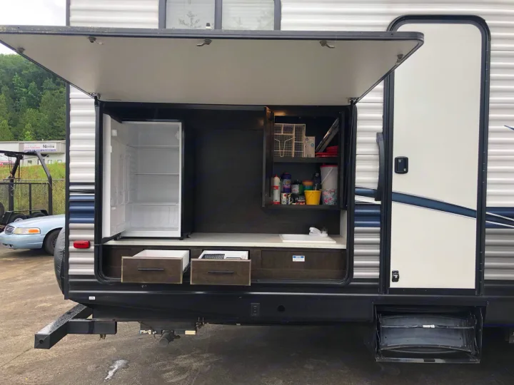 Explore this RV rental's side with its large outdoor kitchen. Includes a mini-fridge, sink, and shelves.. Heartland RVs Prowler 2020