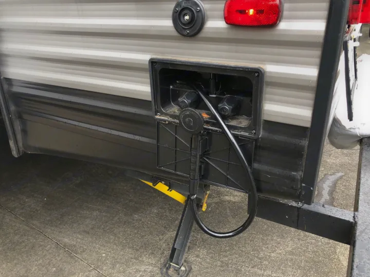 RV rental utility panel showing outdoor shower, water hookups, and stabilizer jack extended on pavement.. Heartland RVs Prowler 2020