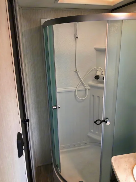 Compact RV rental shower with a curved glass door and handheld showerhead, showcasing functional design.. Heartland RVs Prowler 2020