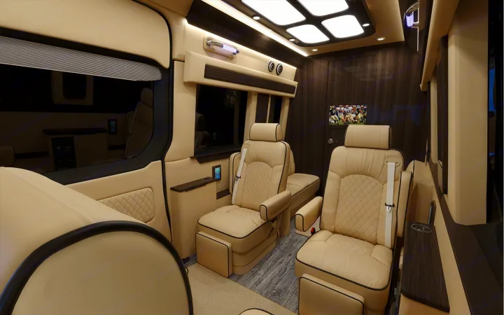 Spacious RV rental interior: luxurious beige leather seats, dark wood trim, ample lighting, and an entertainment screen for comfort.. Ultimate Toys Ultimate Coach 2023