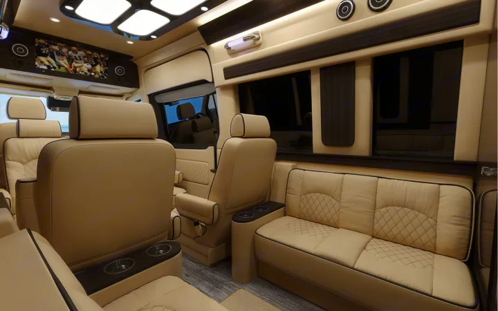 Inside a luxurious RV rental: plush tan leather seating, diamond stitching, a TV, and elegant wood trim offer premium comfort.. Ultimate Toys Ultimate Coach 2023