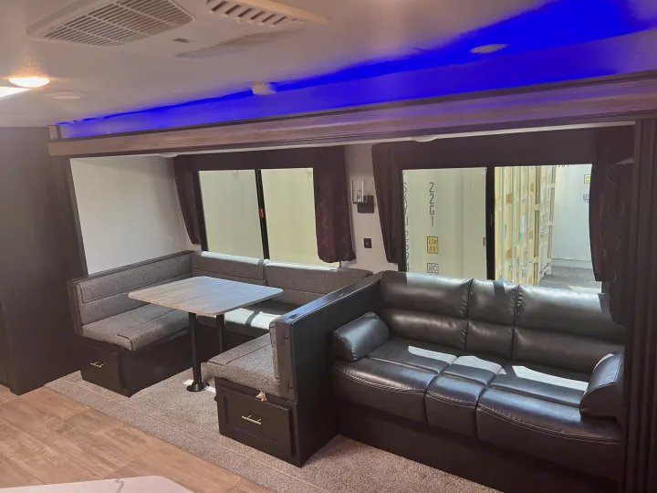 Step inside this cozy RV rental, featuring a dining booth, table, and a comfortable black couch, illuminated by blue accent lighting.. Forest River Cherokee 2021