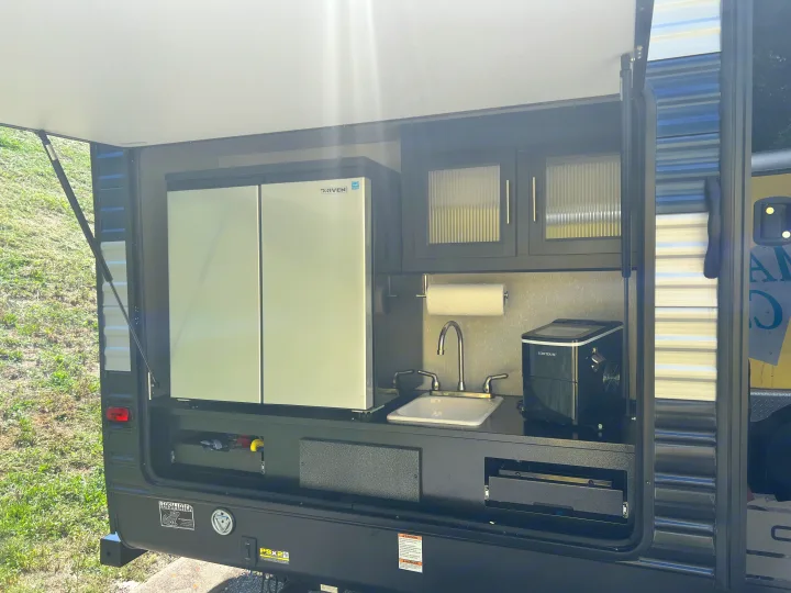 This RV rental's outdoor kitchen, revealed by an open hatch, offers a fridge, sink, ice maker, and cooktop for easy trips.. Forest River Cherokee 2021