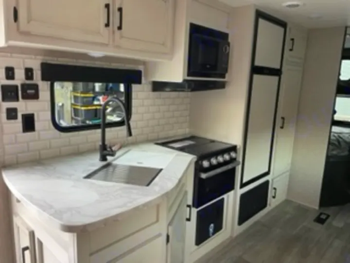 Explore this clean, modern RV rental kitchen interior: white cabinets, sink, stove, microwave, fridge. Ready for adventure!. Jayco Jay Flight SLX 8 2023