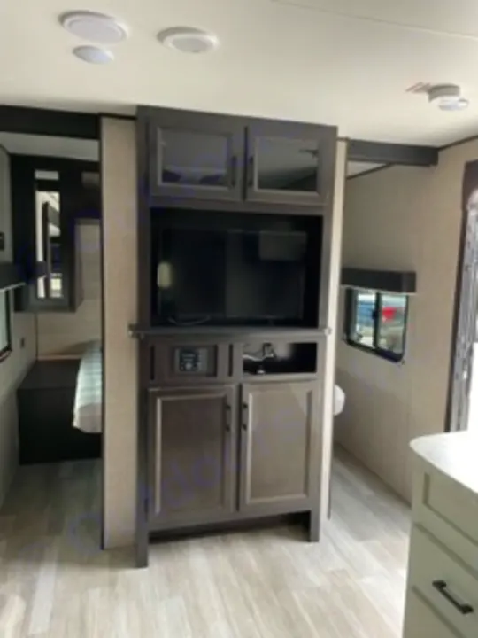 RV rental interior: A dark wood entertainment center with a TV, storage cabinets, and control panel is shown.. Jayco Jay Flight SLX 8 2023
