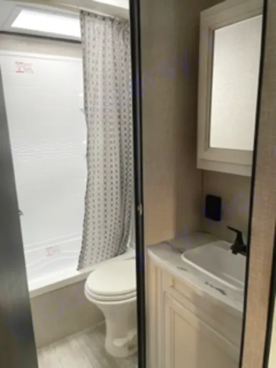 Inside an RV rental bathroom, a compact space with a toilet, shower curtain, and vanity with a sink and overhead skylight.. Jayco Jay Flight SLX 8 2023