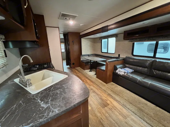 Inside a clean RV rental, featuring a full kitchen with sink, a U-shaped dining booth, and a comfortable sofa.. Jayco Jay Flight 2016