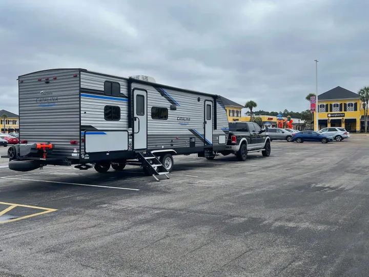 RV rental: A large Coachmen Catalina travel trailer with its tow truck, parked in a shopping center lot on a cloudy day.. Forest River Coachmen Catalina Legacy 2022
