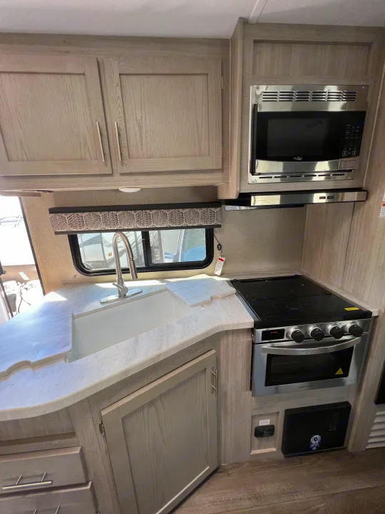 This modern rv rental kitchen boasts light wood cabinets, a stainless steel microwave, range, and sink, ideal for your travels.. Coachmen Catalina 2022