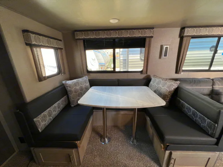 RV rental interior: A cozy U-shaped dinette with comfortable seating, a dining table, patterned valances, and bright windows.. Coachmen Catalina 2022