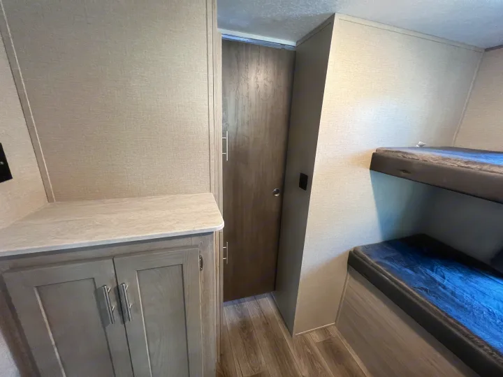 Spacious RV rental interior featuring bunk beds, a storage cabinet with counter, and a door, ideal for family travel.. Coachmen Catalina 2022