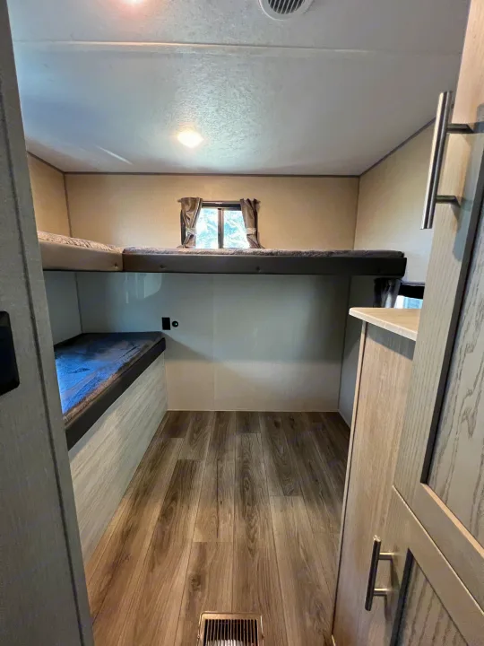 Spacious rv rental bunk room featuring two beds, a window, wood flooring, and bright lighting.. Coachmen Catalina 2022