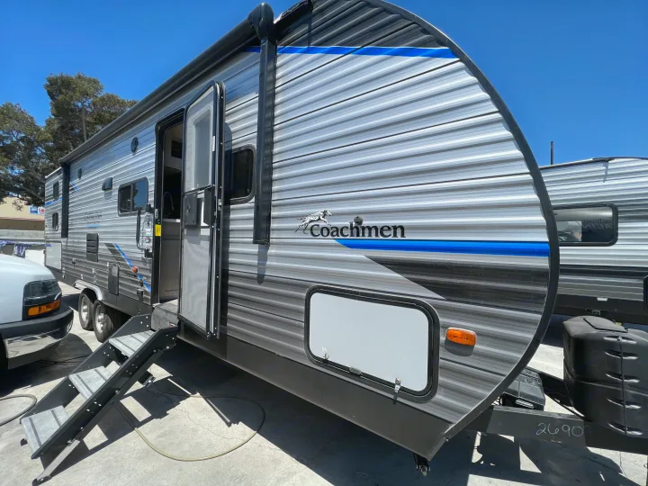 A silver and grey Coachmen travel trailer, with steps down and door open, is ideal for an RV rental adventure under clear skies.. Coachmen Catalina 2022