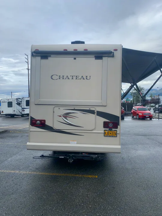 Rear view of a beige Chateau RV rental, showing the license plate KJE 374 and a receiver hitch.. Thor Motor Coach Chateau Sprinter 2018