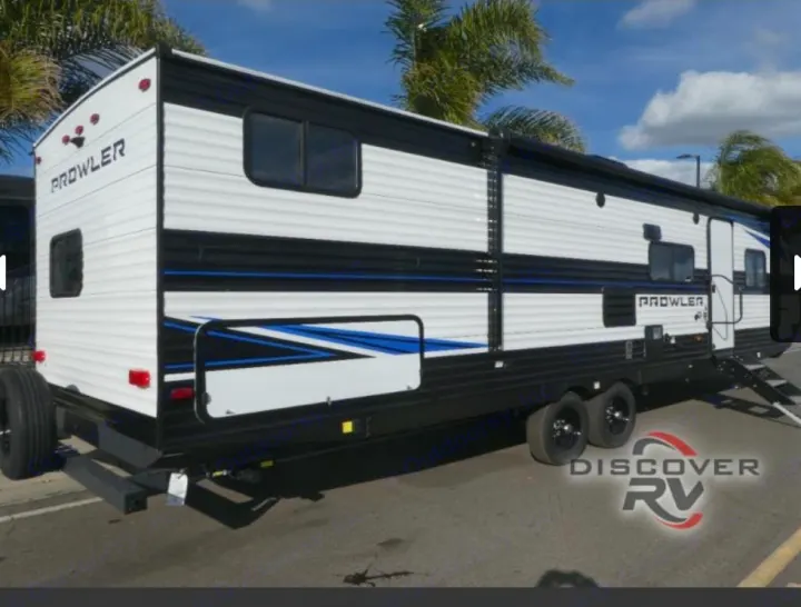This white and black Prowler travel trailer RV rental, featuring blue accents and an awning, is parked outdoors.. Heartland Prowler 2022