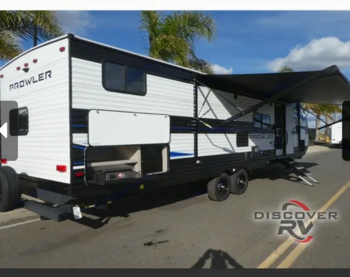 White & black travel trailer RV rental with an open outdoor kitchen and extended awning, parked on pavement.. Heartland Prowler 2022