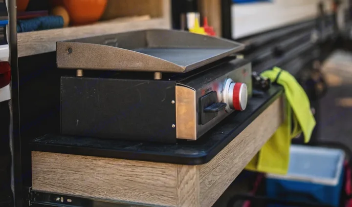 An RV rental's compact outdoor kitchen features a portable griddle on a slide-out stove, perfect for camping meals.. Heartland Prowler 2022