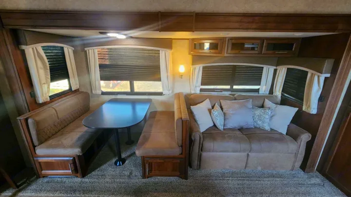 Inside a cozy RV rental: A modern dinette with booth seating, a plush sofa, and windows with blinds offer comfort.. Jayco Eagle HT 2018