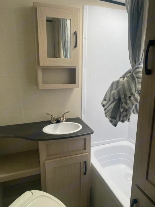 RV rental bathroom with light wood vanity, sink, mirror cabinet, and compact shower/bathtub combo.. Forest River Coachman Apex Nano 2022