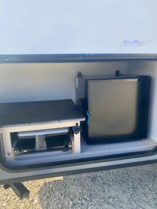 RV rental outdoor kitchen setup. Features a mini-fridge and pull-out shelf for cooking appliances in a side compartment.. Forest River Coachman Apex Nano 2022