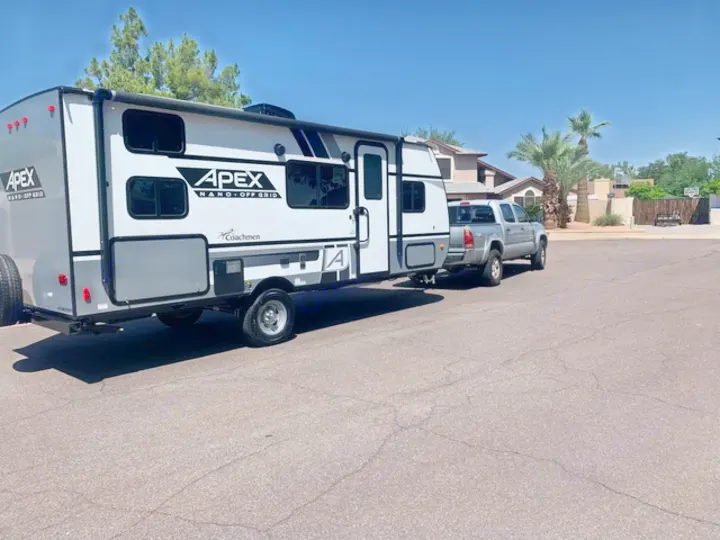A white & gray travel trailer is hitched to a silver pickup truck on a sunny street. Perfect for an RV rental trip!. Forest River Coachman Apex Nano 2022