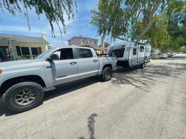 Grey truck towing an Apex travel trailer, an rv rental, parked on a sunny residential street. Ready for adventures!. Forest River Coachman Apex Nano 2022