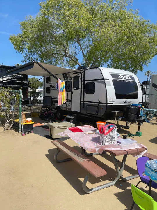 Sunny day at an RV rental campsite: a Coachmen Apex travel trailer with awning, picnic table, and gear.. Forest River Coachman Apex Nano 2022