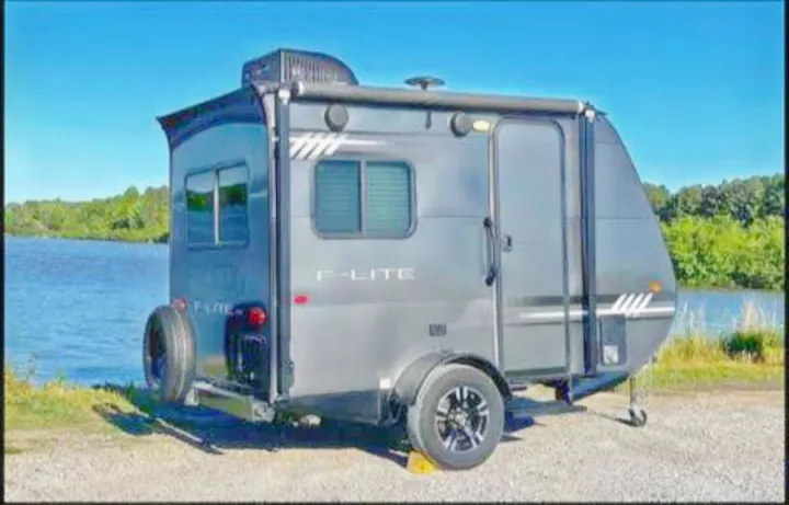 Gray F-Lite travel trailer by a lake, perfect for an RV rental. This compact RV offers lakeside camping and adventure.. Travel Lite Falcon 2019