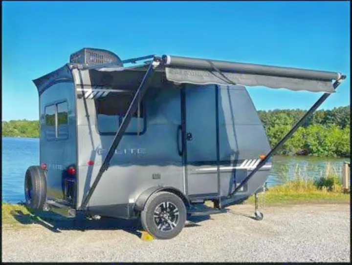 Gray teardrop RV rental with awning extended by a lake, perfect for camping trips.. Travel Lite Falcon 2019