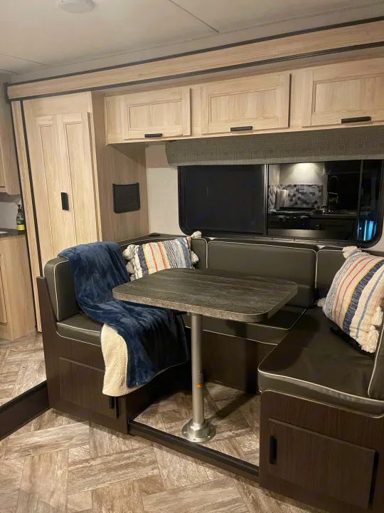 RV rental dinette: dark U-shaped seating with blanket, table, light wood cabinets. Cozy interior.. Forest River Sunseeker LE 2022