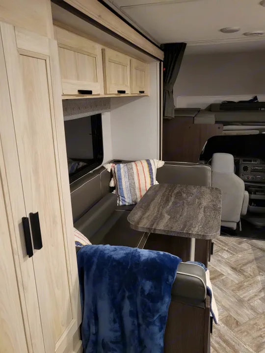 This RV rental features a comfortable dinette with dark cushions, light wood overhead cabinets, and a forward sleeping area.. Forest River Sunseeker LE 2022