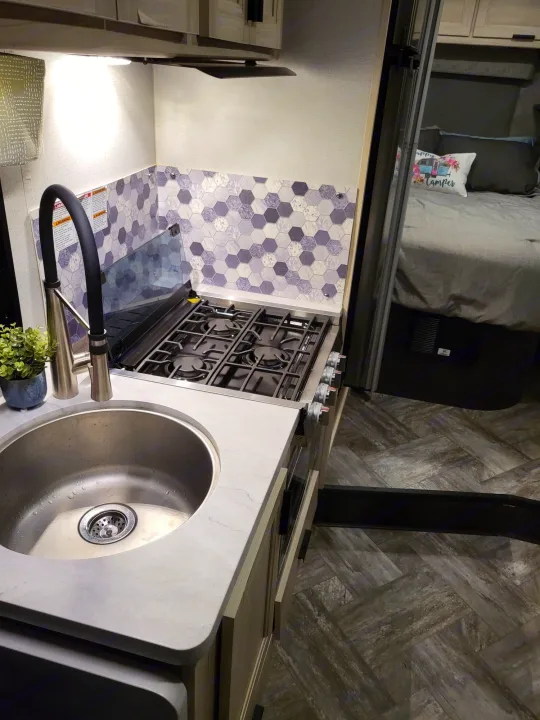 Explore this modern RV rental! Features a clean kitchen with sink, stove, and hexagonal backsplash, plus a comfy bedroom.. Forest River Sunseeker LE 2022