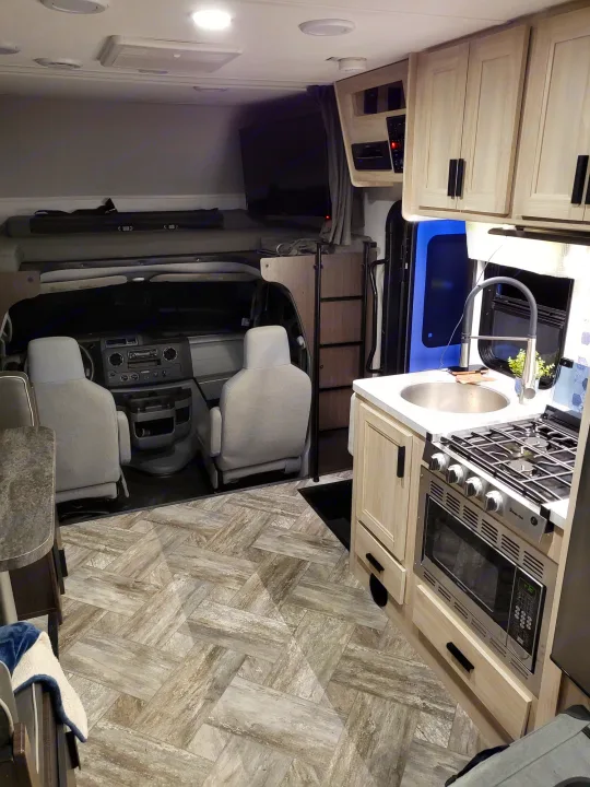 Inside a modern RV rental: well-equipped kitchen, driver's cab, and front bunk. Light wood-look flooring extends throughout.. Forest River Sunseeker LE 2022