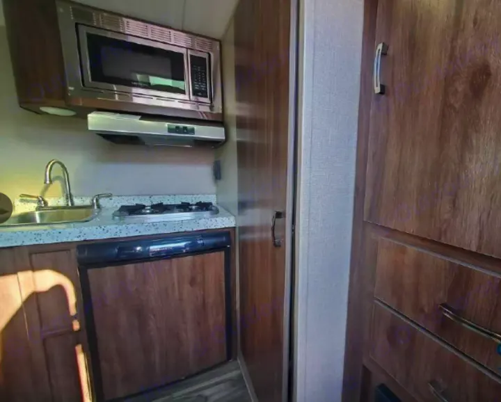 A well-equipped kitchen inside an RV rental, featuring a microwave, sink, two-burner stove, and compact refrigerator.. Travel Lite Falcon 2019