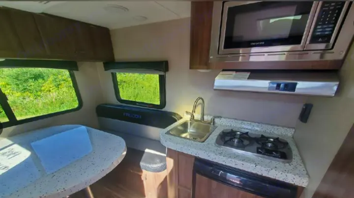 Compact RV rental interior featuring a kitchen with sink, stove, microwave, and a dining area with scenic window views.. Travel Lite Falcon 2019