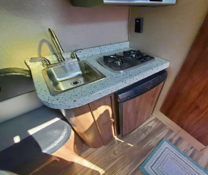 Inside an RV rental: a practical kitchenette with sink, two-burner stove, and compact fridge.. Travel Lite Falcon 2019