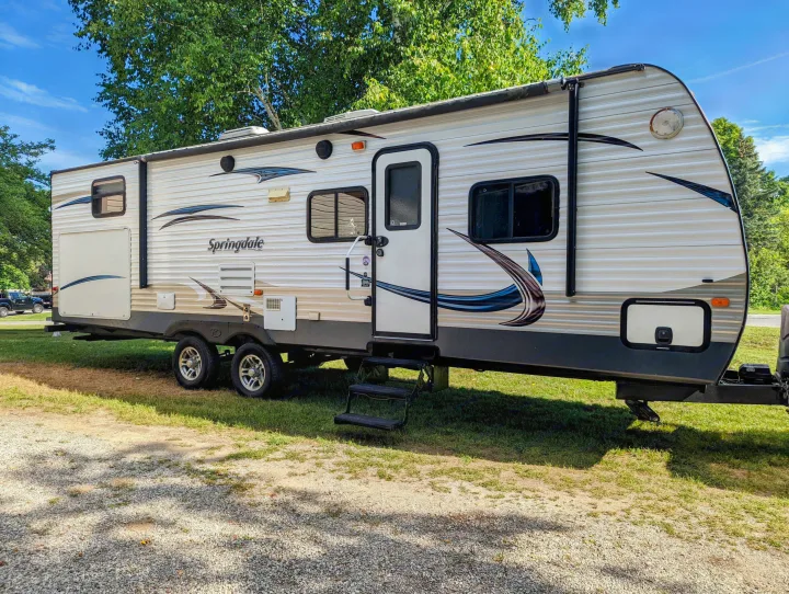 This Springdale travel trailer, a great RV rental option, is parked on a sunny grassy campsite with trees overhead.. Keystone RV Springdale 2013