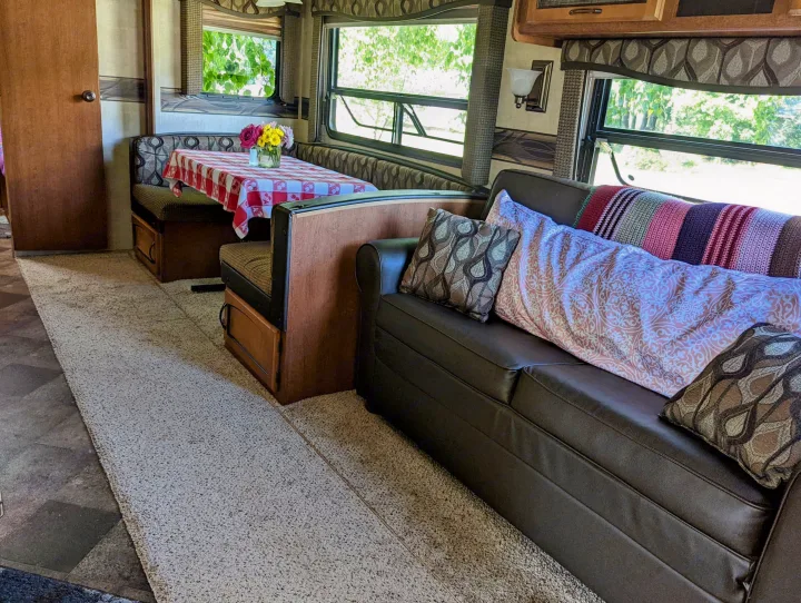 RV rental interior: cozy dinette with flowers, sofa with pillows, and bright windows showing green trees.. Keystone RV Springdale 2013
