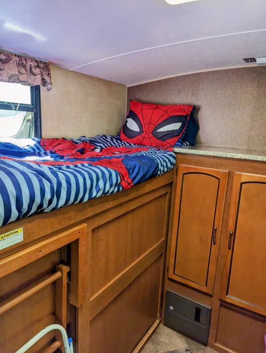 Cozy RV rental bunk bed with Spider-Man bedding, wooden cabinets, and a window. Ideal for family adventures.. Keystone RV Springdale 2013
