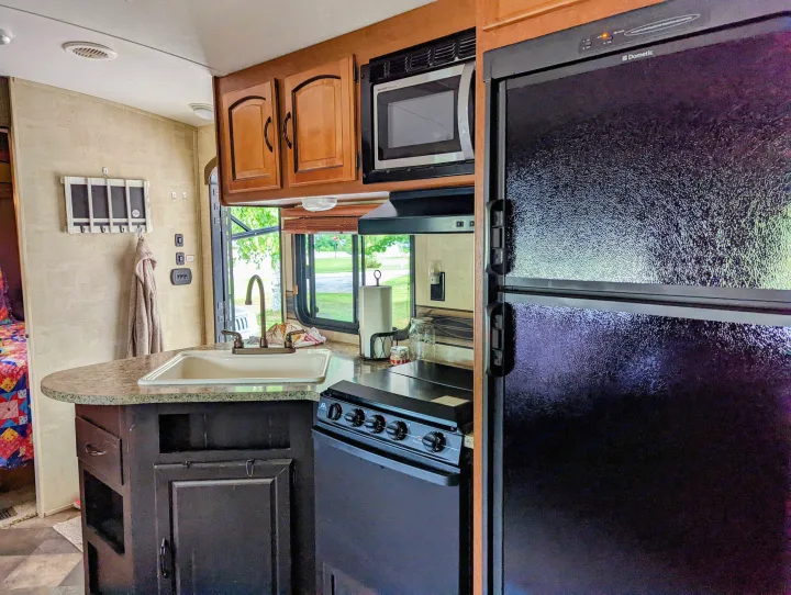 Experience comfort in this RV rental kitchen, complete with a sink, microwave, stove, and Dometic refrigerator.. Keystone RV Springdale 2013