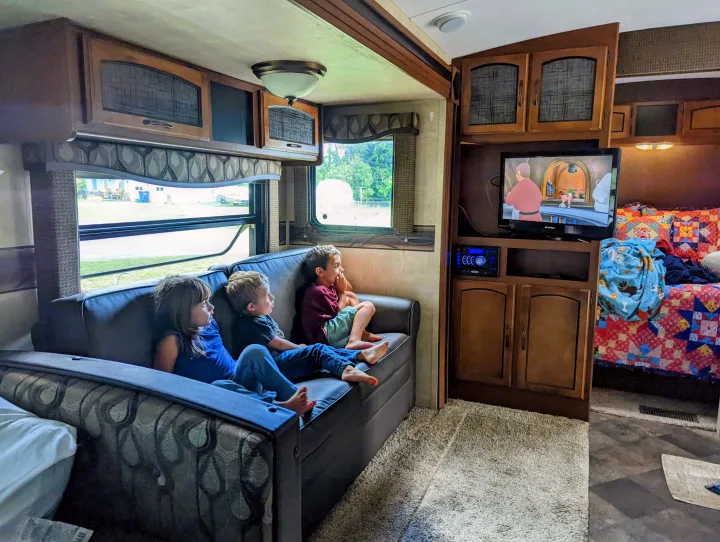 Three kids relax on a sofa watching cartoons on TV inside a cozy RV rental. Ideal for family trips!. Keystone RV Springdale 2013