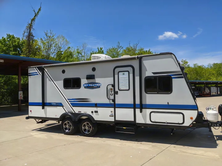 Modern Jay Feather travel trailer, ideal for an rv rental. It's grey/white with bold blue stripes, parked on sunny concrete.. Jayco Jay Feather 2019