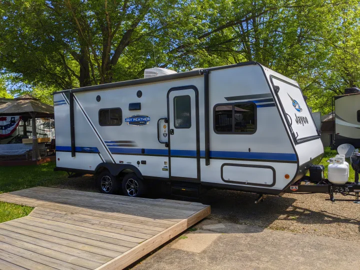 Jayco Jay Feather RV rental, parked on gravel next to a wooden deck at a shaded campsite.. Jayco Jay Feather 2019