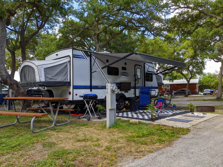 Relaxing RV rental getaway: a modern travel trailer with awning, grill, and picnic area at a shaded campsite.. Jayco Jay Feather 2019