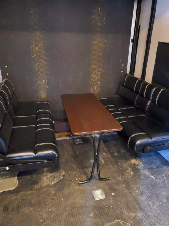 RV rental interior: black faux-leather benches & brown table form a dining area. Wall scuffs resemble tire marks.. Forest River Vengeance 2018