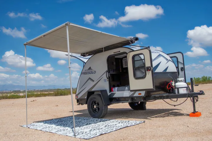 Compact Freesolo RV rental travel trailer set up for outdoor camping. Awning extended in a sunny desert scene.. Braxton Creek Free Solo 2022